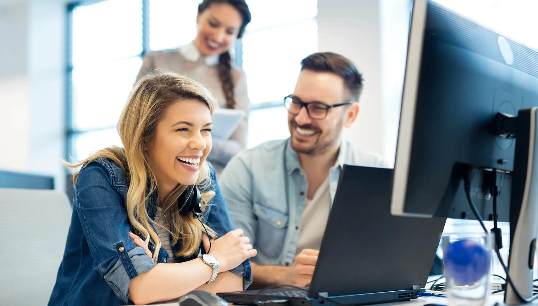 Two colleagues laughing together at a computer