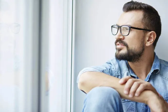 A man sitting by a window, looking out thoughtfully