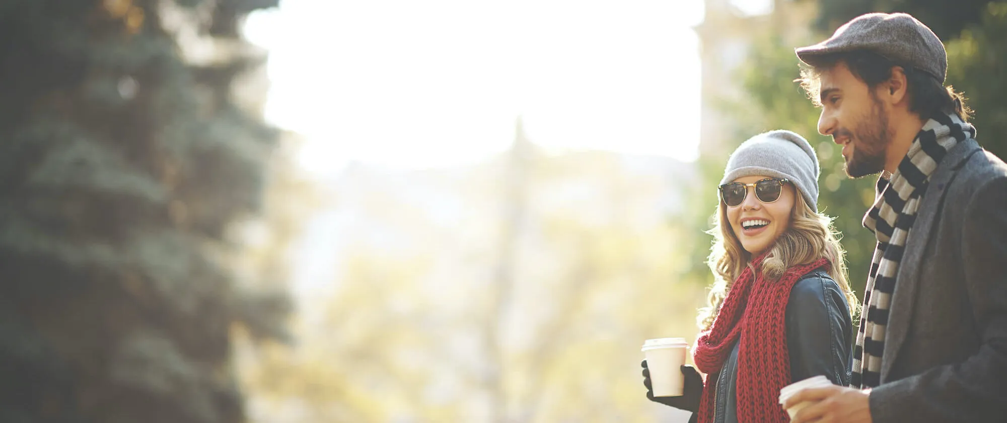 A smiling couple walking outdoors together with takeaway coffees