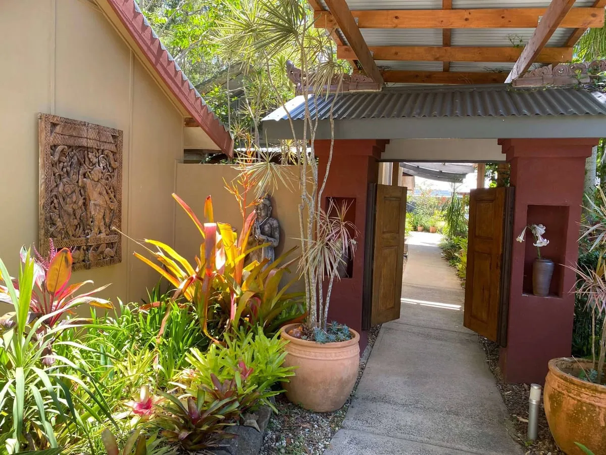 A garden path at Sangsurya leading through an open timber gateway, lined with bromeliads and a carved wall panel
