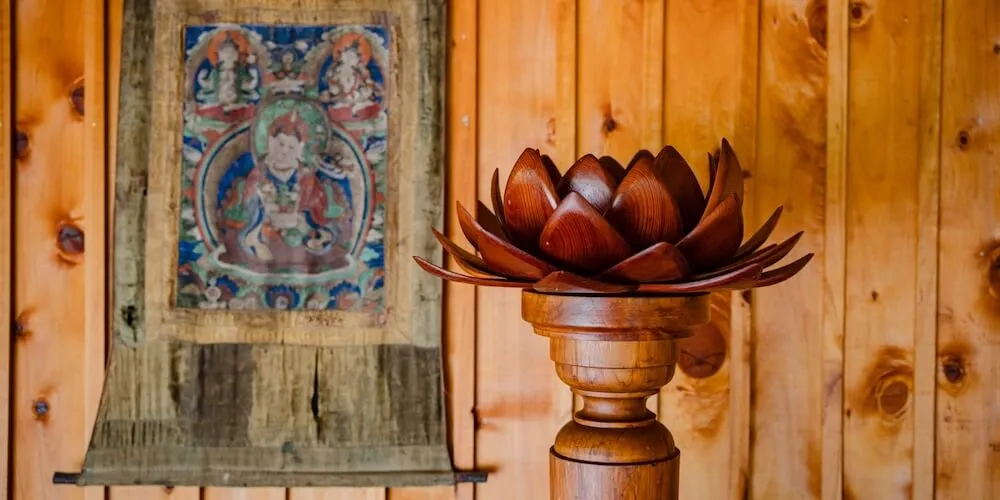 A carved wooden lotus on a stand in front of a Tibetan thangka painting at Te Moata
